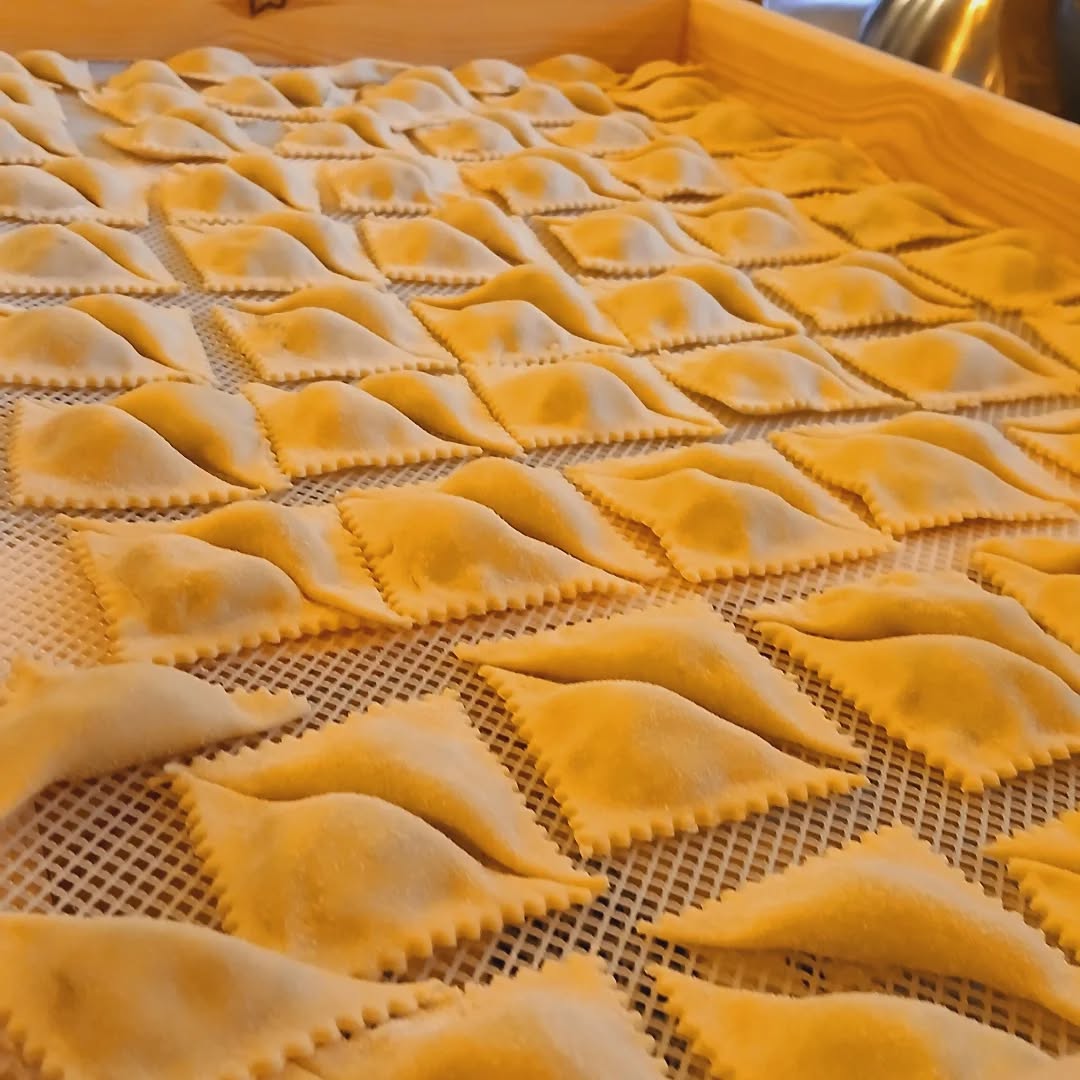 Paste ripiene dai bordi dentellati in file ordinate su griglia bianca dentro un vassoio di legno, preparate da Buò