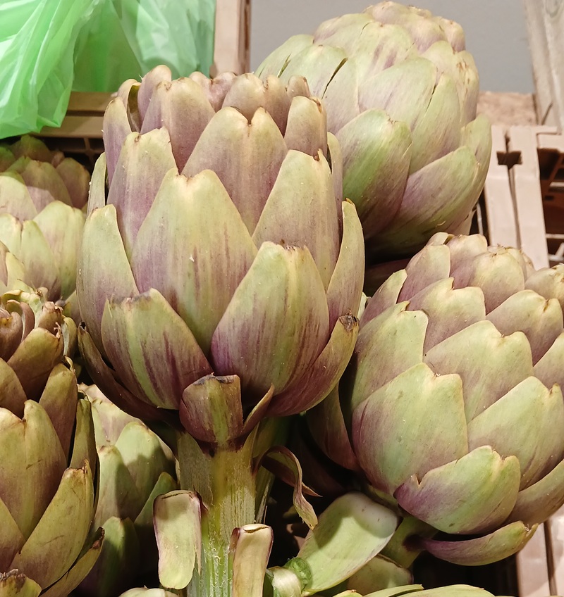 Carciofi violetti con gambo e foglie verdi in cassette di legno sul banco verdure di Buò